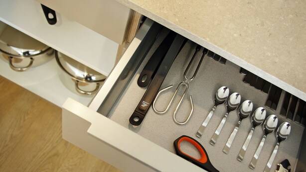 Un cajón con diversos utensilios de cocina, incluyendo tijeras, cucharas y un cuchillo.
