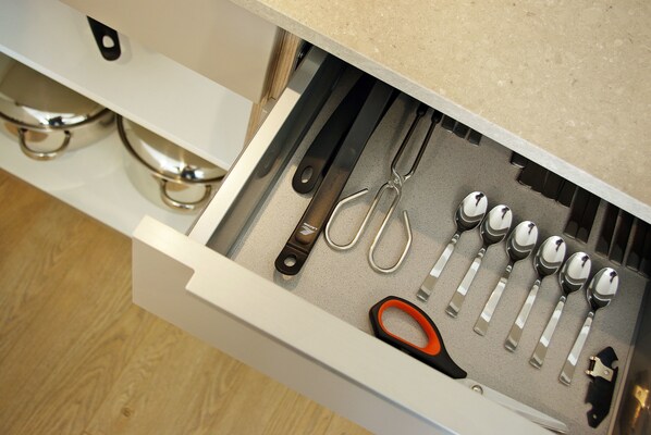 Un cajón con diversos utensilios de cocina, incluyendo tijeras, cucharas y un cuchillo.