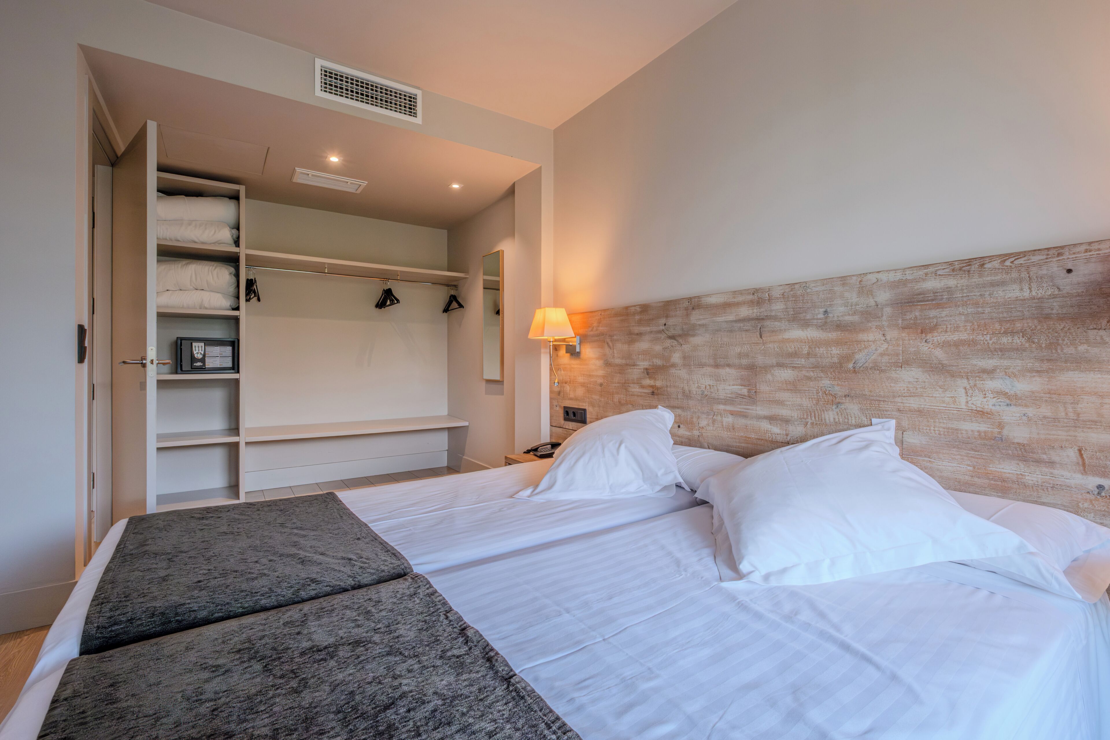 A hotel room with a bed, a wardrobe, a bedside table, and a lamp.