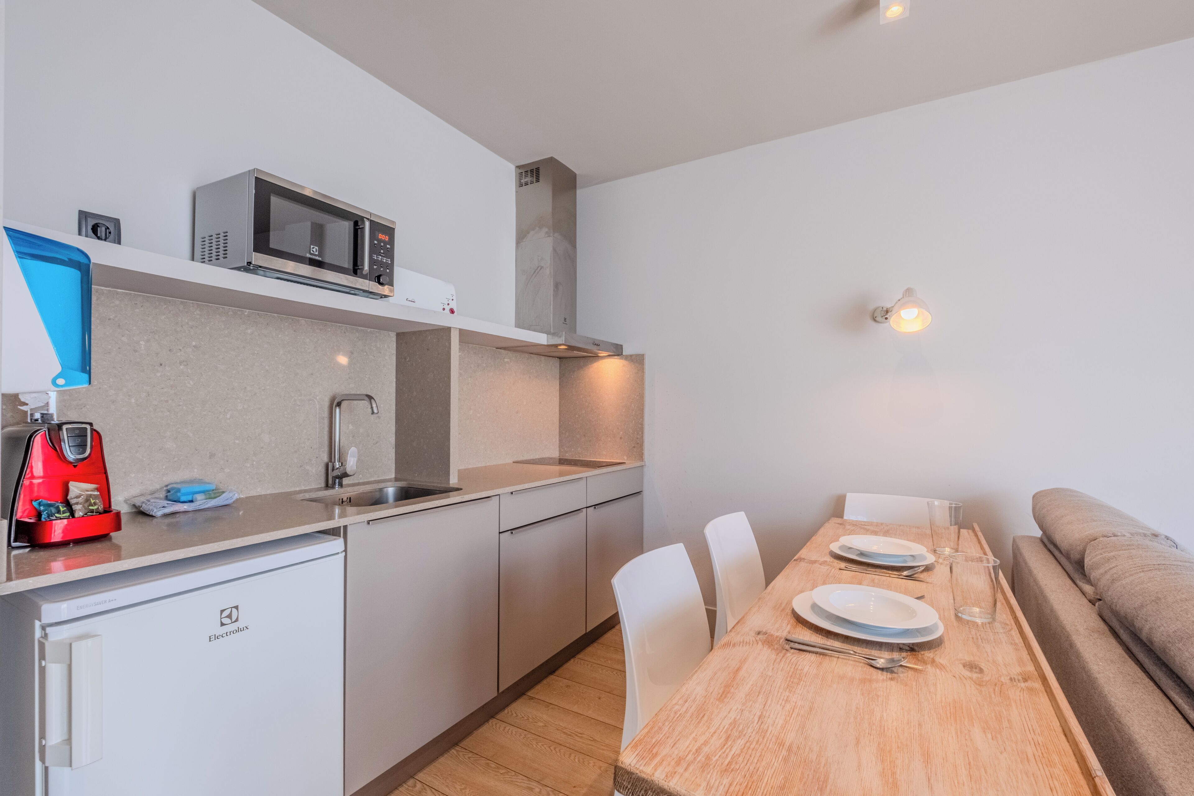 A compact kitchenette with a microwave, sink, and a red coffee machine.