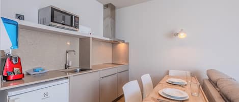 A compact kitchenette with a microwave, sink, and a red coffee machine.