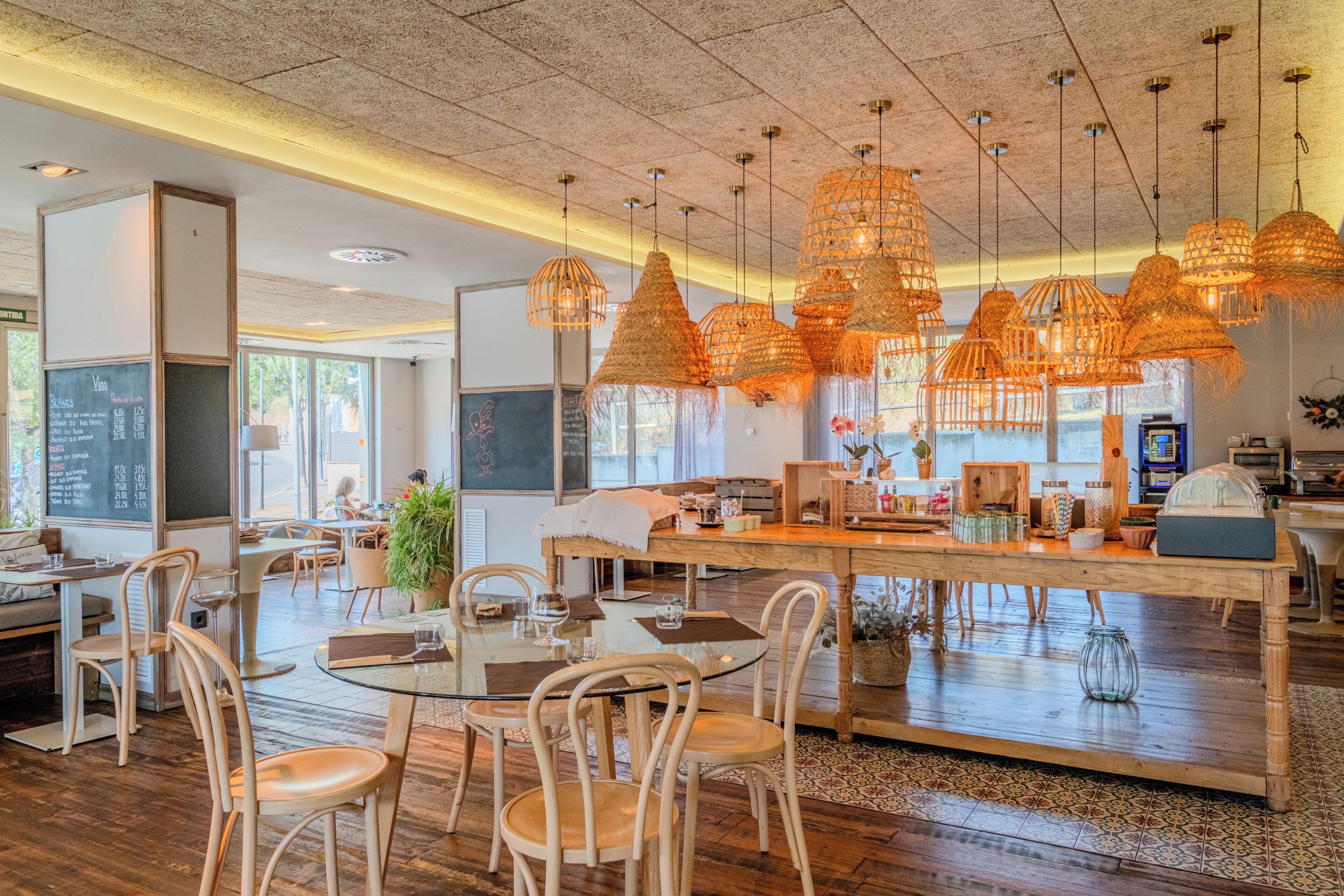 Un restaurante con piso de madera, mesas redondas, lámparas colgantes de mimbre y un menú en la pizarra.