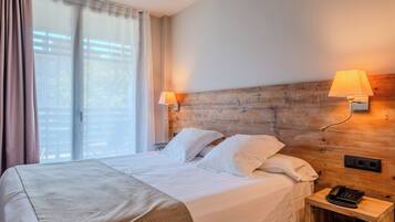 A hotel room with a bed, two bedside lamps, a wooden headboard, a window with curtains, and a bedside telephone.