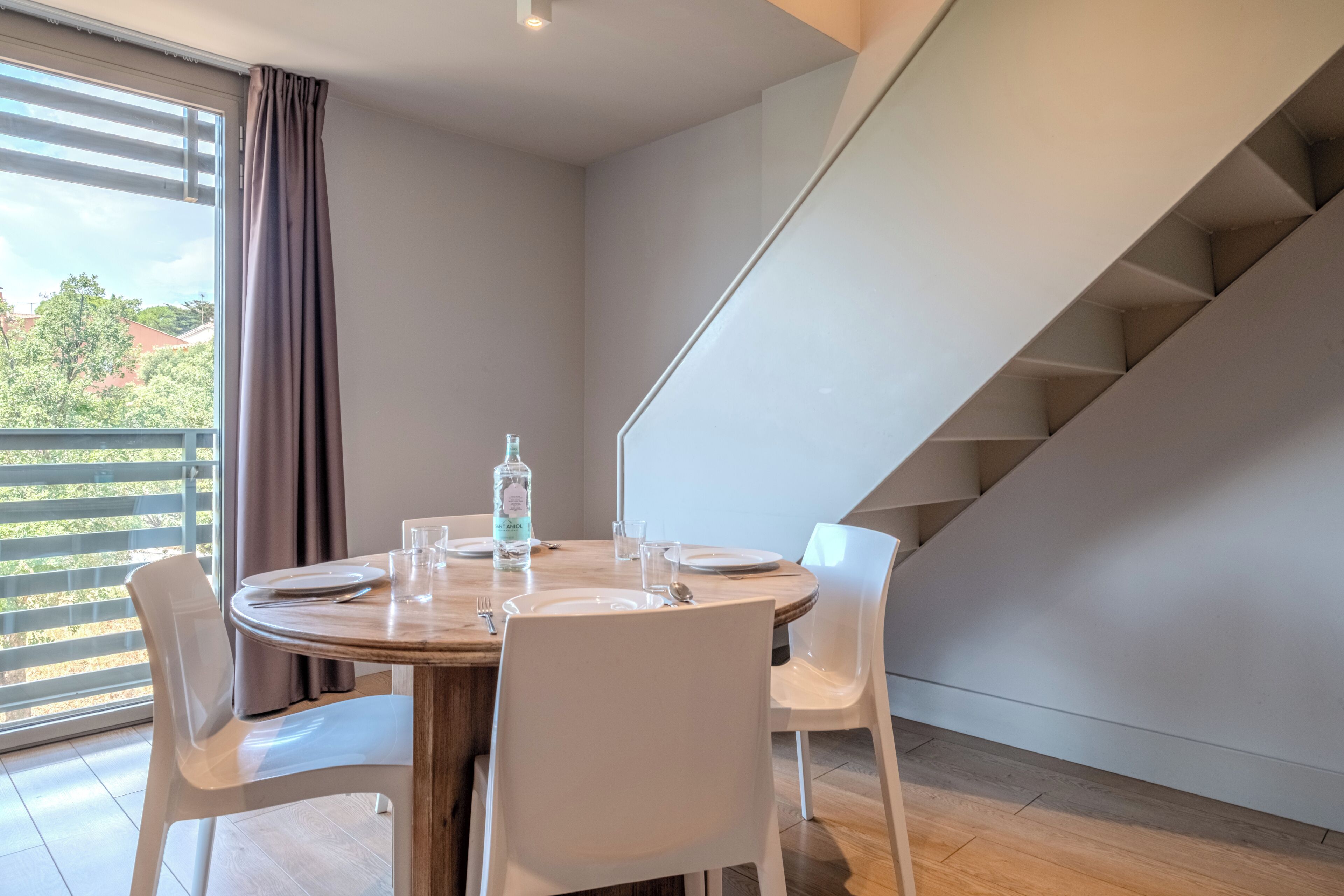 Een eethoek met een ronde tafel, witte stoelen, een waterfles en een glas op tafel.