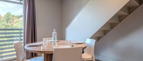 A dining area with a round table, white chairs, a bottle of water, and a glass on the table.