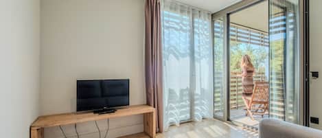 A modern living room with a flat-screen TV on a wooden bench, a grey sofa, and a sliding glass door leading to an outdoor area.