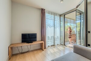 Una sala moderna con un televisor de pantalla plana sobre un banco de madera, un sofá gris y un ventanal corredero que da a un área exterior.