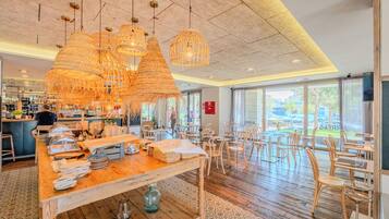 Interior de un restaurante con barra de madera, lámparas colgantes de fibra y vista a través de grandes ventanales.