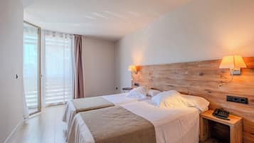 Una habitación de hotel con cabecera de madera, dos camas, una mesita de noche con lámpara y un teléfono.