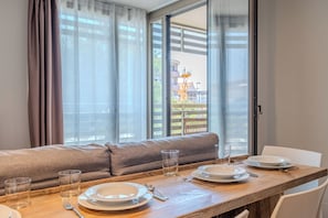 Un comedor con una mesa de madera dispuesta para dos, un sofá y vistas a un edificio con una grúa.