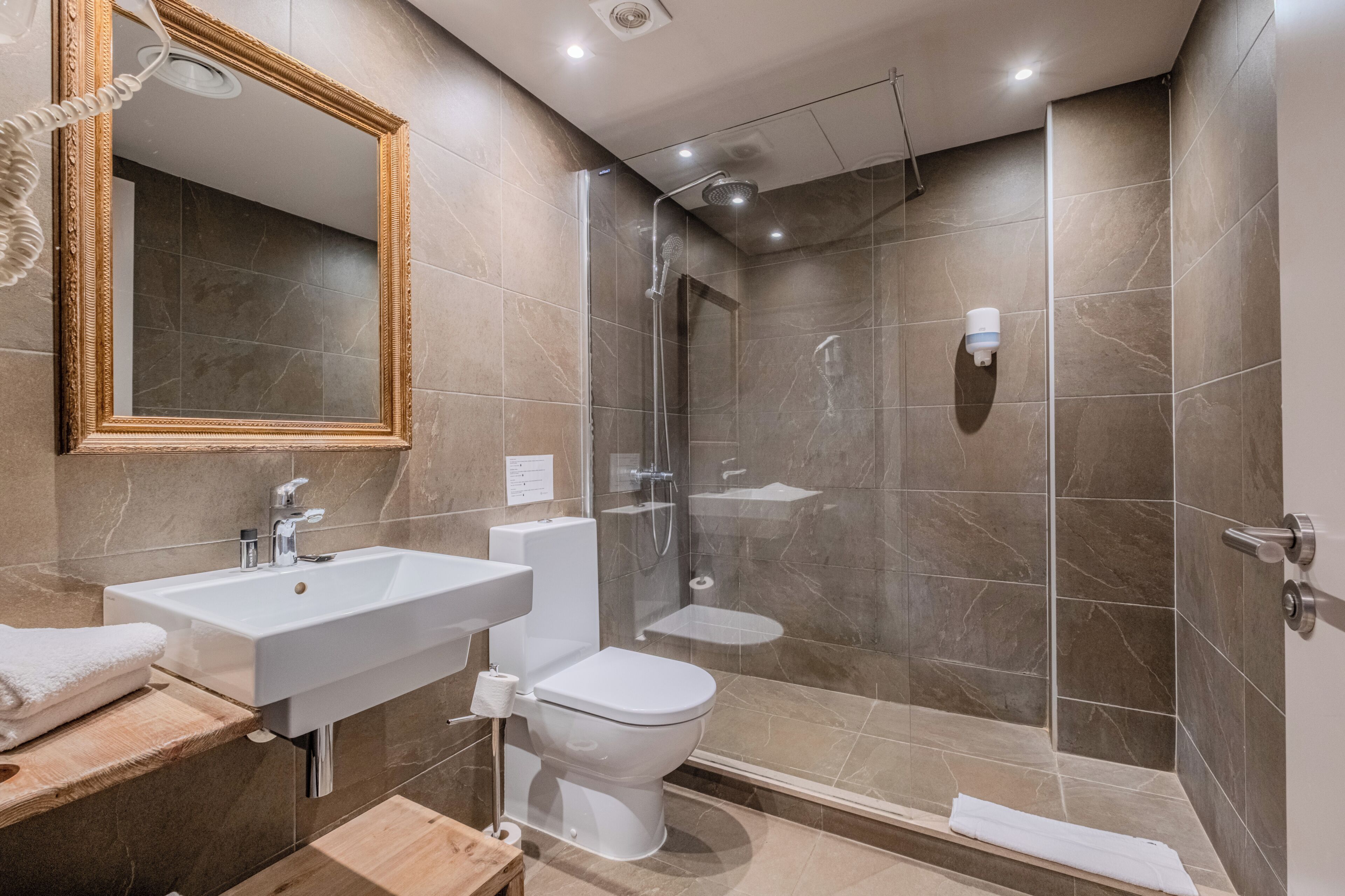 Un baño moderno con un espejo grande, ducha, inodoro y lavamanos.