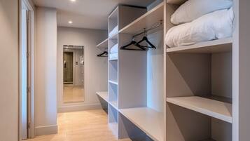 Un vestidor amplio con estantes abiertos y espacio para colgar, suelo de madera y una puerta que da a un baño.