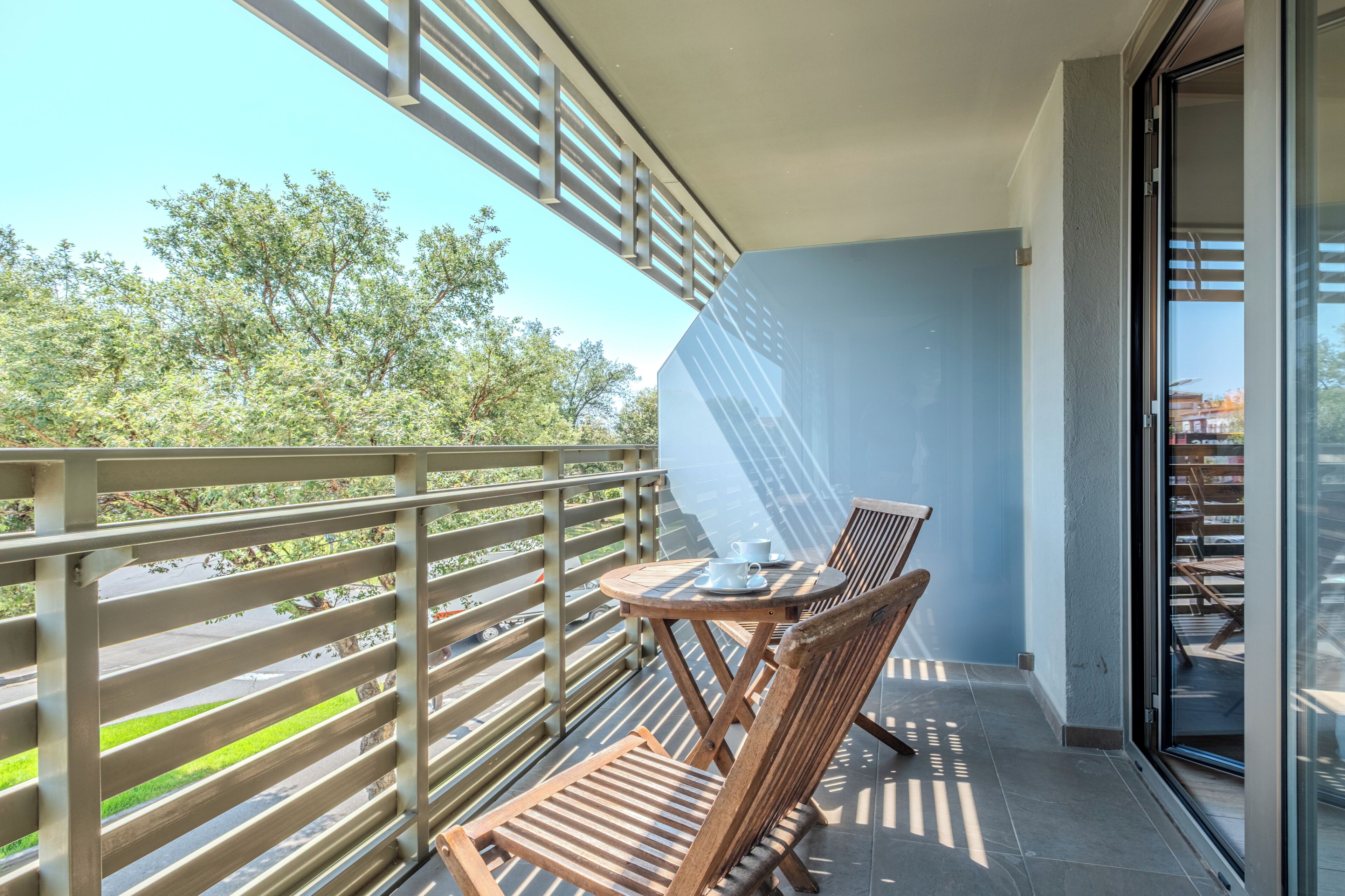 A balcony with a table and chairs, a glass door, and a view of trees.