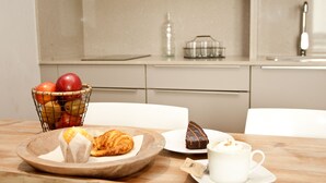 Un desayuno con una cesta de fruta, un croissant, pastel de chocolate y una taza de café sobre una mesa de madera.