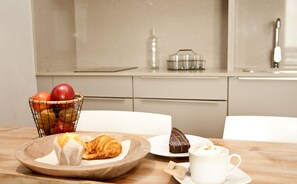 Un desayuno con una cesta de fruta, un croissant, pastel de chocolate y una taza de café sobre una mesa de madera.