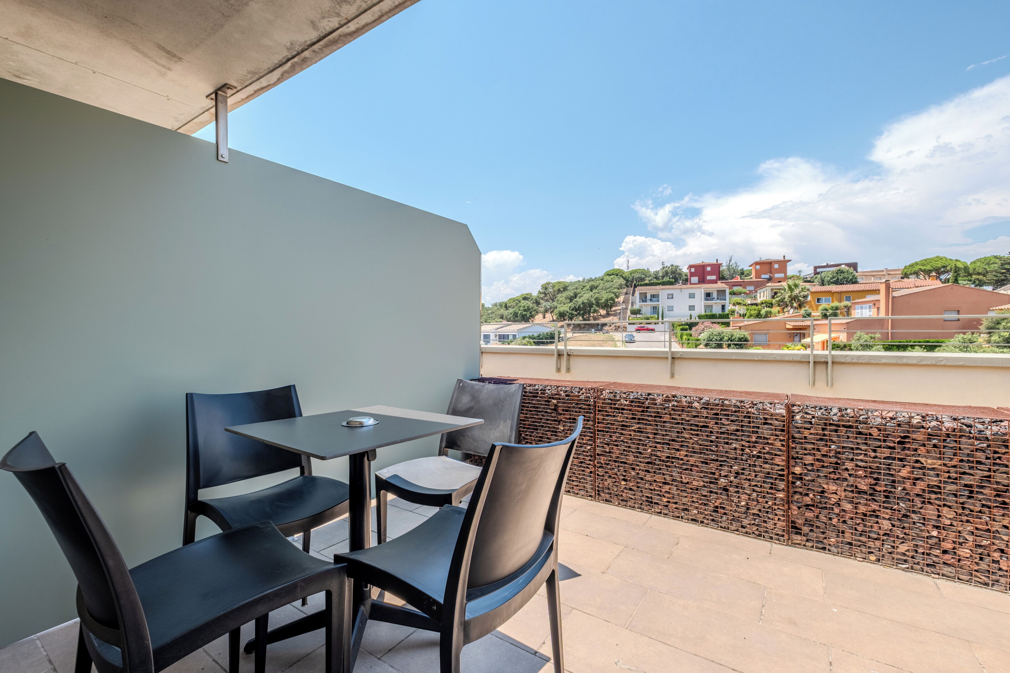 Ein Balkon mit Tisch und Stühlen, mit Blick auf eine Wohngegend mit Häusern und Bäumen.