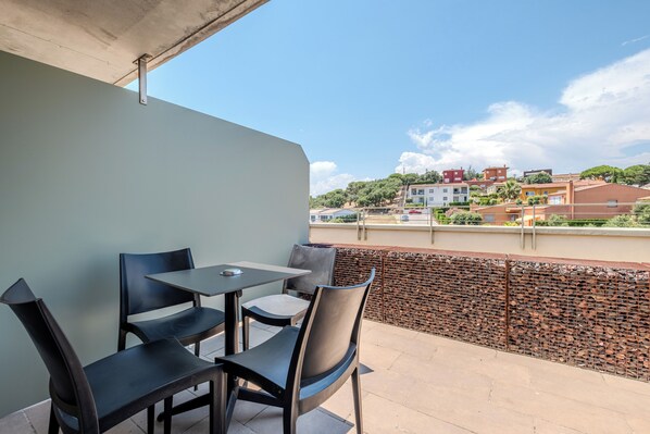 A balcony with a table and chairs, overlooking a residential area with houses and trees.