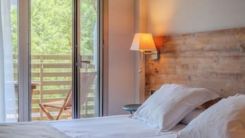 Un dormitorio con cama, almohadas, cabecera de madera, mesita de noche, lámpara y vistas al verdor a través de una puerta corrediza.