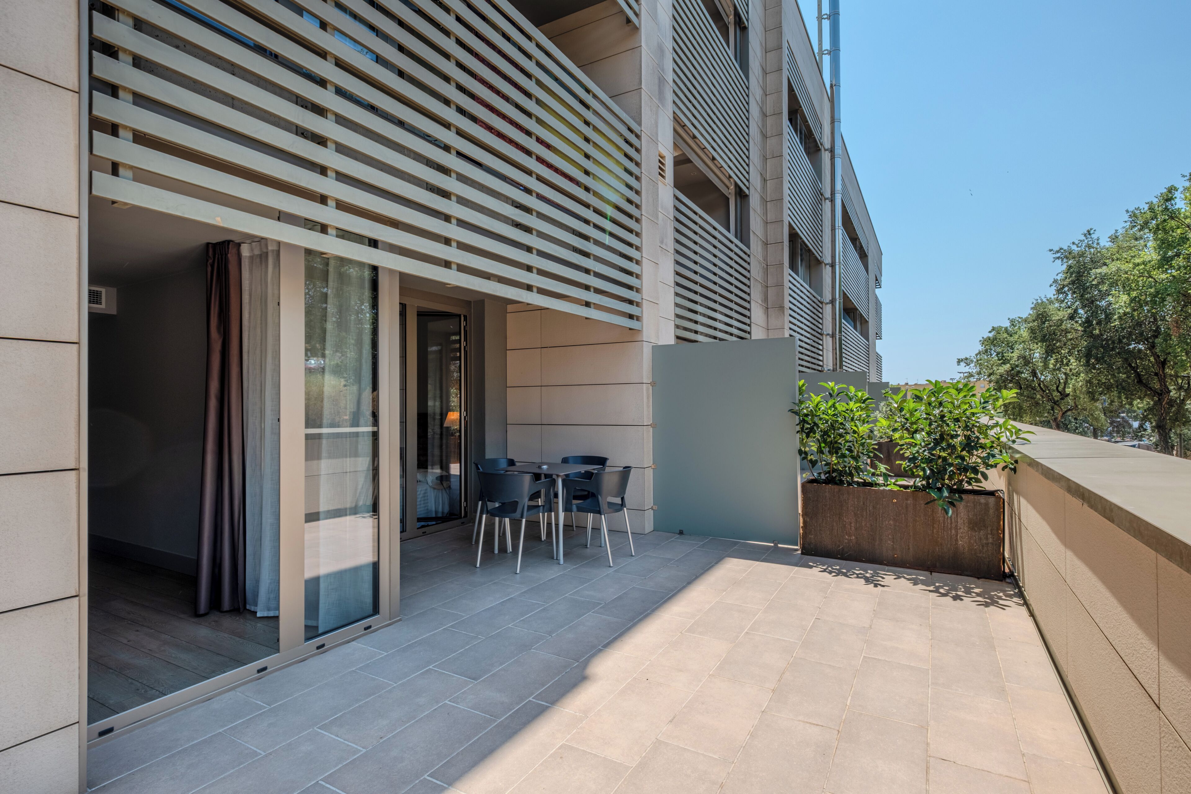 Un espacio al aire libre con patio, una mesa, sillas, una puerta corrediza de vidrio y una jardinera con plantas.