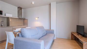 A modern living space with a grey sofa, a wooden coffee table, a TV, and a kitchen area with a stove and cabinets.