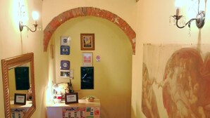Ein schmaler Korridor mit einem Ziegelbogen, einem Empfangstresen mit Spiegel, einem Stuhl und einer Wand mit einem großen abstrakten Gemälde.