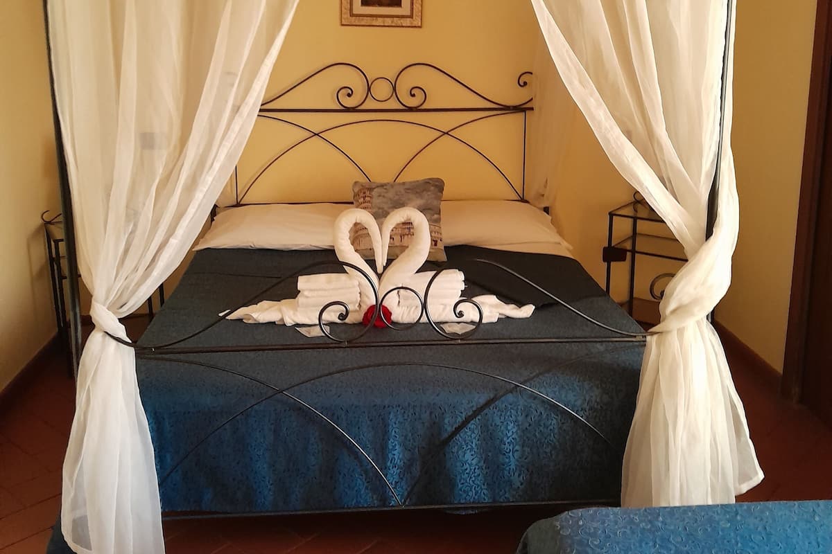A bed with a blue bedspread, white curtains, and a decorative swan made of towels.