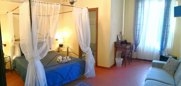 A bedroom with a four-poster bed, a bedside table with a lamp, a chair, and a sofa. - B&B Window To The Tower (Pisa)