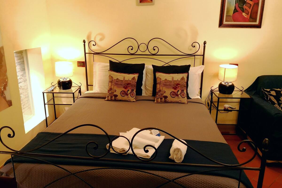 A neatly made bed with two pillows, a bedside table with a lamp, and a chair.