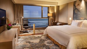 Hotelkamer met een groot bed, een bureau met computer, een televisie en uitzicht op de oceaan.