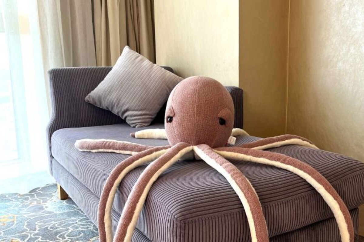 A room with a sofa, a large octopus plush toy, and a window with curtains.