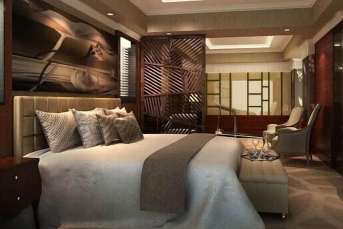A modern bedroom with a large bed, a seating area, and a decorative wall panel.