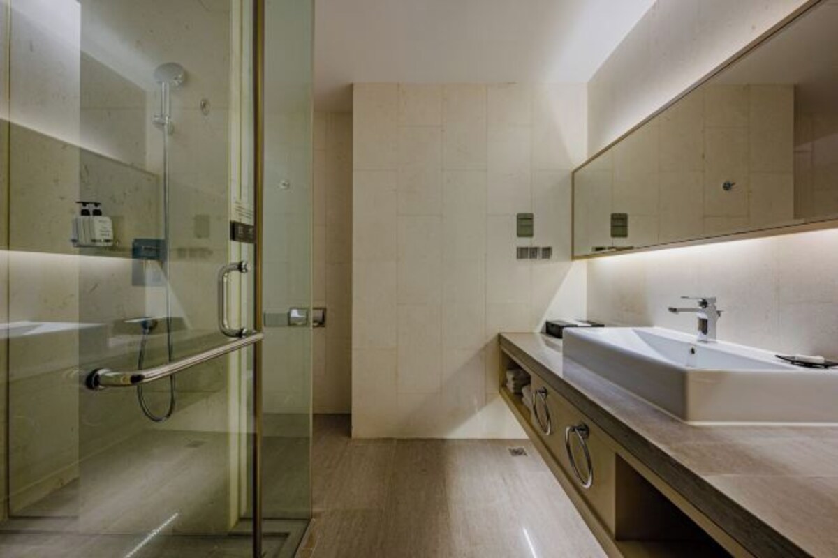 A modern bathroom with a glass shower enclosure, a large mirror, and a countertop with a sink and vanity.