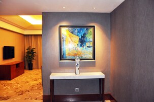 Habitación de hotel con un cuadro enmarcado sobre un lavamanos, un televisor en la pared y una planta en la esquina.