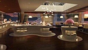 Een moderne hotellobby met een centraal receptiegedeelte, meerdere zithoeken en een hoge plafond met ingebouwde verlichting.