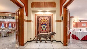 Un pasillo con un escudo en la pared, una estatua de león y mesas preparadas para comer.
