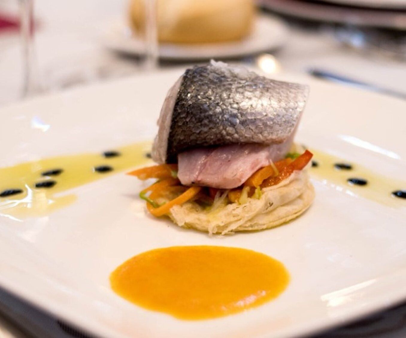 Un plato con pescado, carne y verduras, acompañado de salsa.
