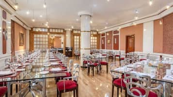 A spacious dining hall with long tables and chairs, a central column, and a wooden floor.