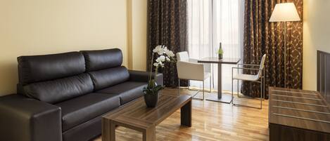 A modern living room with a leather sofa, a wooden coffee table, a potted orchid, a dining table with chairs, and a TV mounted on the wall.