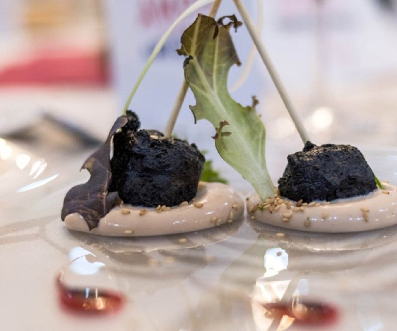 Two dishes with soil and greens on a reflective surface.