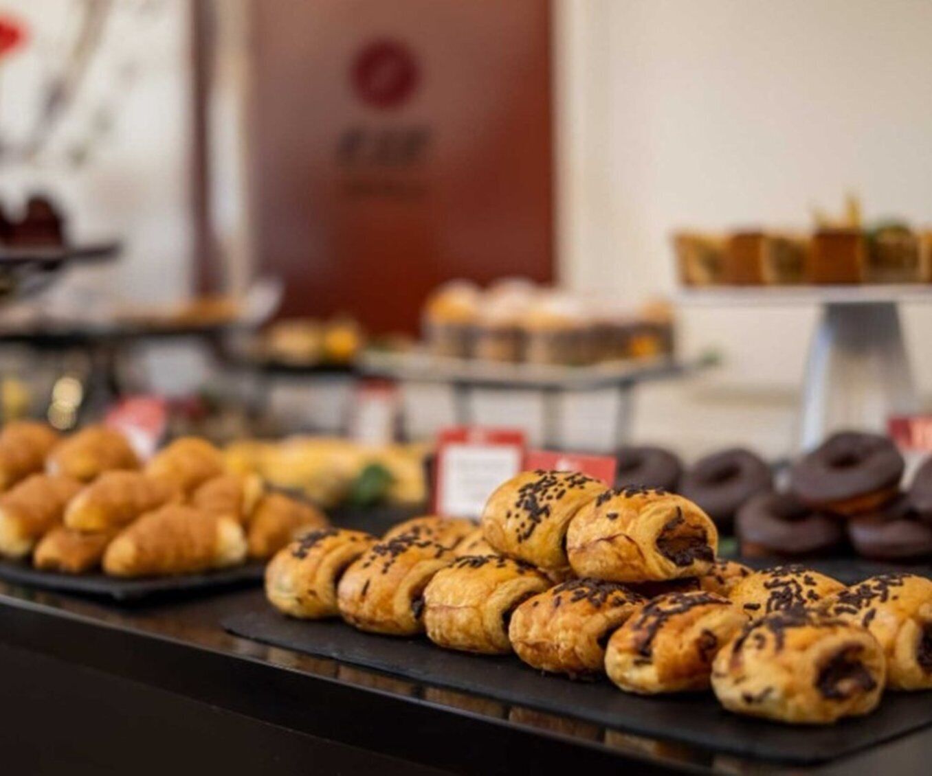 Une variété de produits de boulangerie, notamment des croissants et des pâtisseries enrobées de chocolat, sont présentés sur un comptoir.