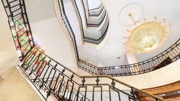 Un interior de varios niveles con una escalera espiral, una lámpara decorativa y un papel tapiz estampado.