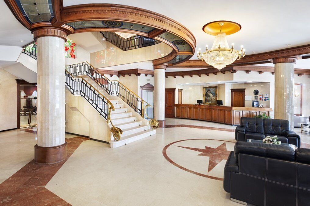 A grand lobby with a central staircase, a chandelier, and a reception desk.