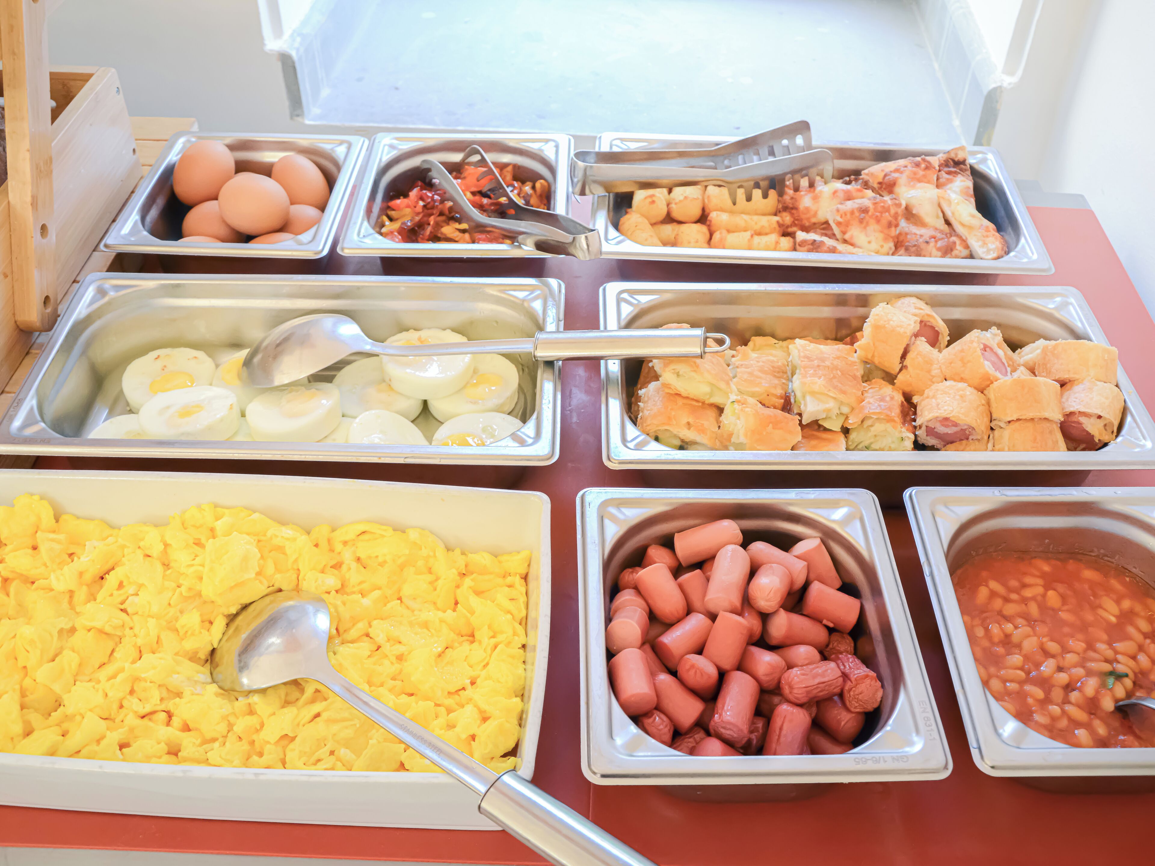 Buffet com diversas opções de comida, incluindo ovos, salsichas e feijão.