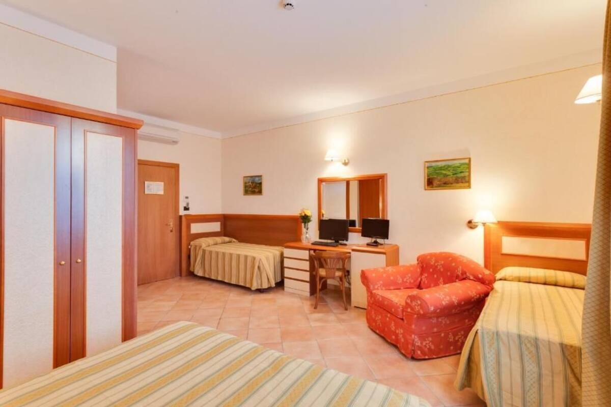 A hotel room with two single beds, a desk with a computer, a chair, a small table, and a wardrobe.