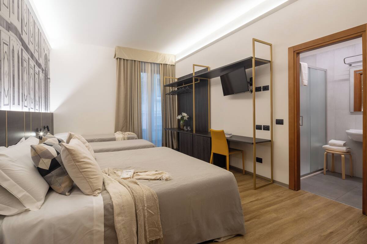 A hotel room with a bed, a desk, a chair, a TV, and a bathroom.