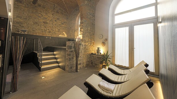 Ein Wellnessbereich mit Steinwänden, einer Treppe und sonnendurchfluteten Liegestühlen.