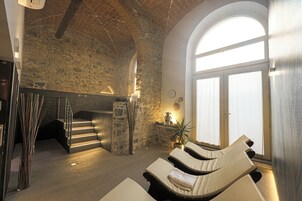 Area benessere con pareti in pietra, una scala e poltrone prendisole illuminate dal sole.