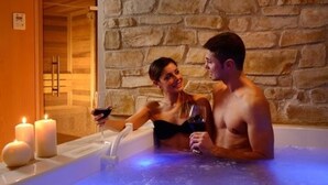 Ein Paar in einer Badewanne mit Kerzen und einer Steinsäule im Hintergrund.