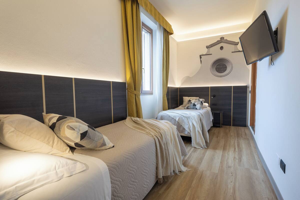 A hotel room with two beds, a TV mounted on the wall, and a window with curtains.