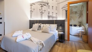 Ein modernes Hotelzimmer mit einem großen Bett, einem kleinen Nachttisch, einem Badezimmer mit Badewanne und Blick auf eine Stadtlandschaft durch eine Glastür.